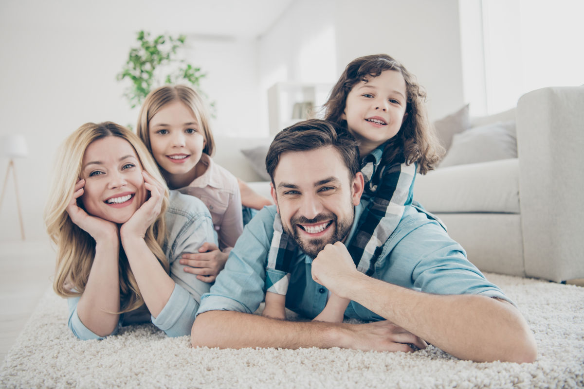 Familie liegt lachend im Wohnzimmer auf dem Boden