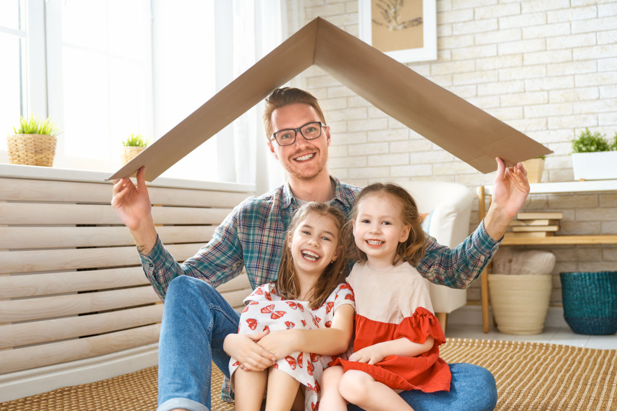 Vater mit zwei Kindern hält ein Kartondach über ihre Köpfe
