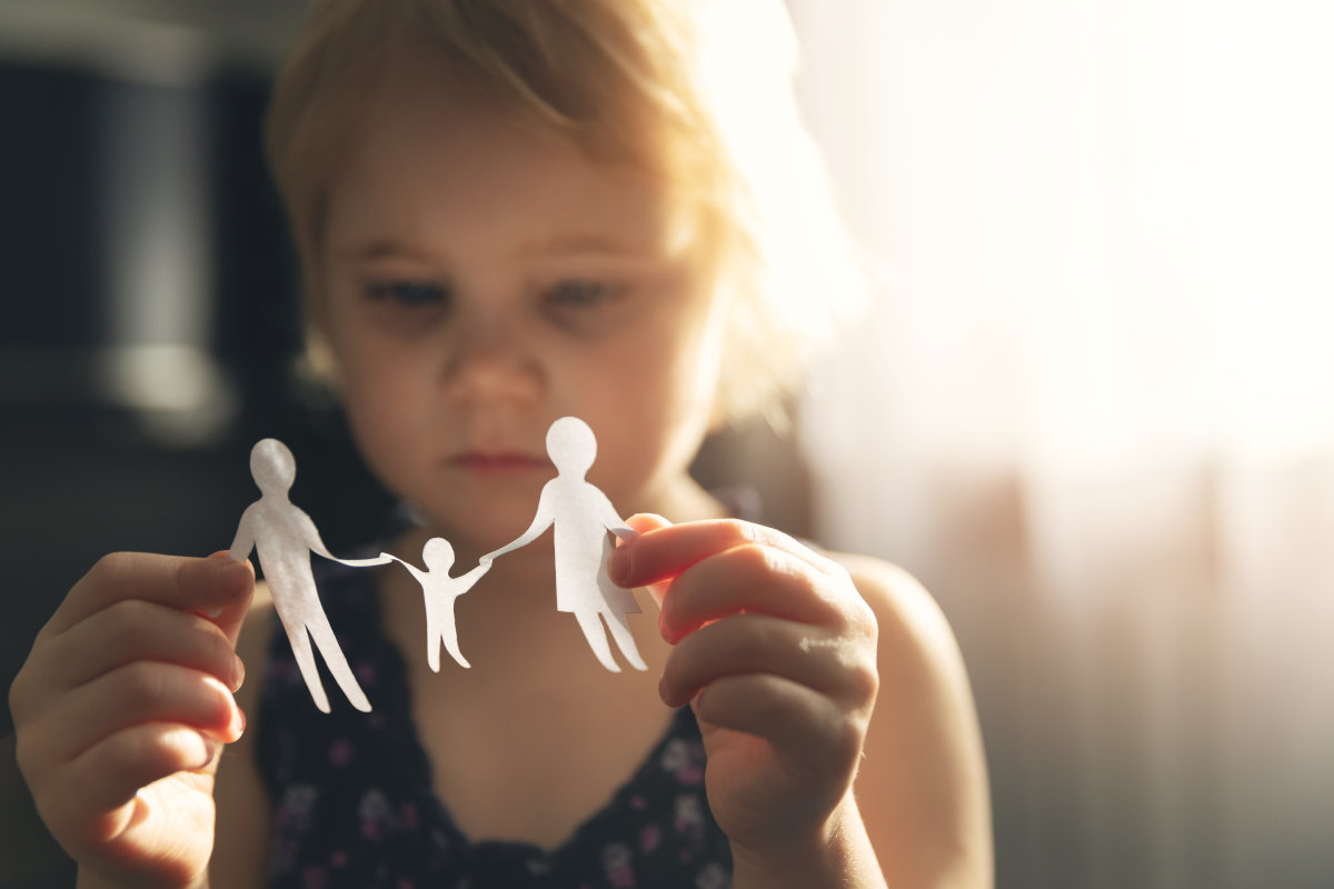 Kind hält Papierfiguren einer Familie in den Händen
