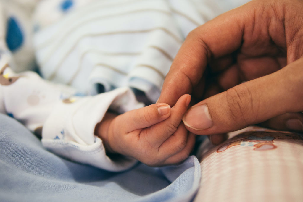 Mann hält Finger von neugeborenem Baby